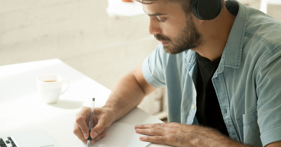Homem escrevendo no papel. Nesse artigo, conheça quais são as vantagens em converter áudio em texto.